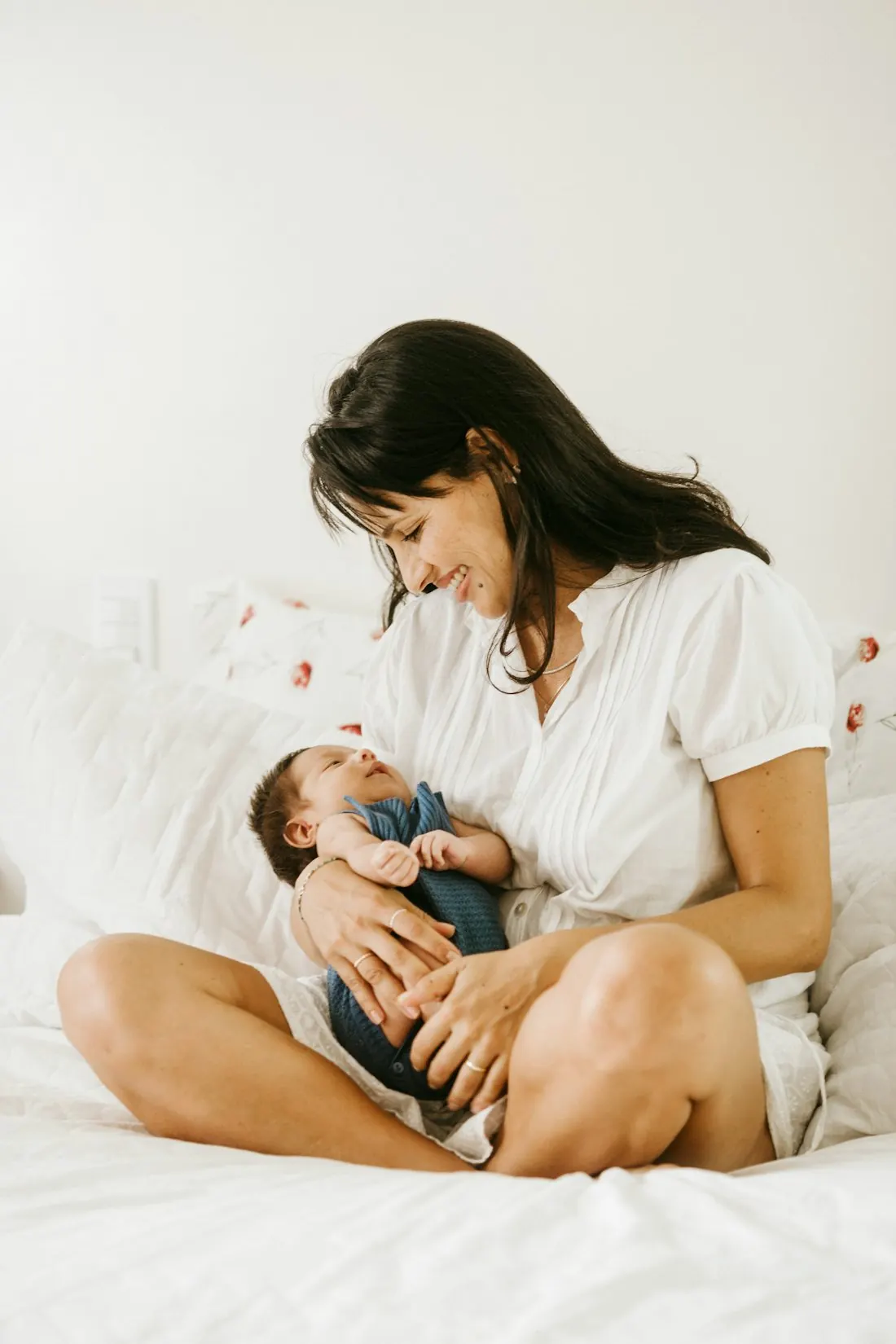 Una madre sentada en la cama sostiene a su bebé recién nacido dormido